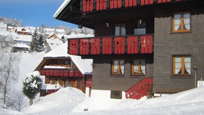 Ein Hotel mit einem roten Balkon, verschneiter Umgebung und Blick auf andere Gebäude im Hintergrund.