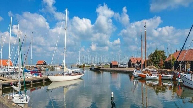 A marina with multiple boats docked, calm water, and buildings with red roofs.
