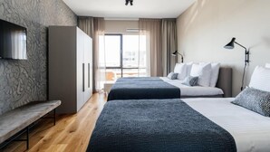 A modern hotel room with two beds, a bench, a TV, and a large window with curtains. - Harbor Retreat, Scheveningen (Scheveningen)