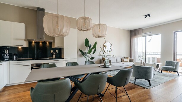Une cuisine moderne avec des meubles blancs, un îlot central doté de chaises, des luminaires suspendus et une grande fenêtre qui laisse entrer la lumière naturelle.