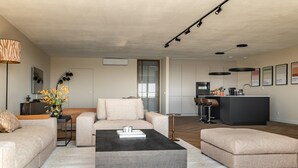 Un salon moderne avec un canapé, un pouf et une table basse. Il y a également un coin cuisine avec un bar et une table à manger.