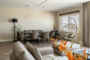 A modern living room with a dining area, a hanging chair, and a large window with blinds.