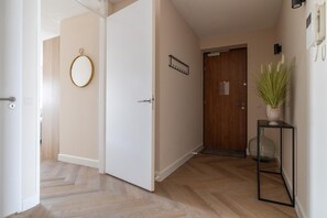 A hallway with a wooden door, a white wall with a circular mirror, and a potted plant on a small table.