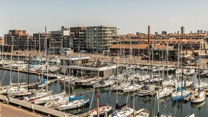 Un port de plaisance où sont amarrés de nombreux bateaux, entouré de bâtiments modernes et sous un ciel dégagé.