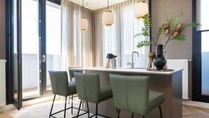 Une cuisine moderne dotée d’un îlot central, de trois tabourets de bar, de luminaires suspendus et offrant une vue dégagée grâce à de grandes fenêtres.