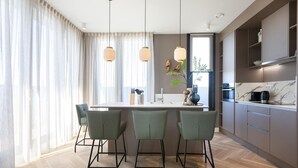 Une cuisine moderne dotée d’un îlot central, de tabourets de bar, de luminaires suspendus et offrant une vue sur l’extérieur.