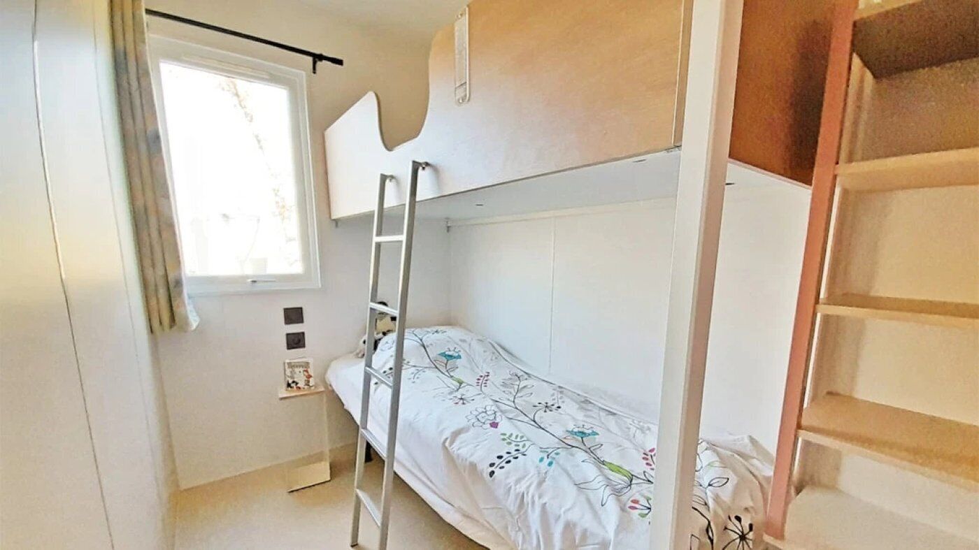 Een kleine kamer met een enkel bed en een stapelbed, een raam met gordijnen, en een trap.