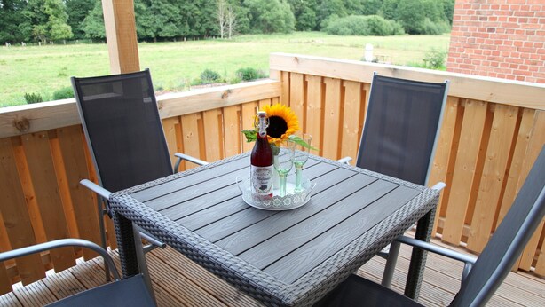 A wooden deck with a table and chairs, a bottle of wine, and a glass of water on the table. - Ferienwohnung mit Terrasse, Bad Bodenteich (Bad Bodenteich)