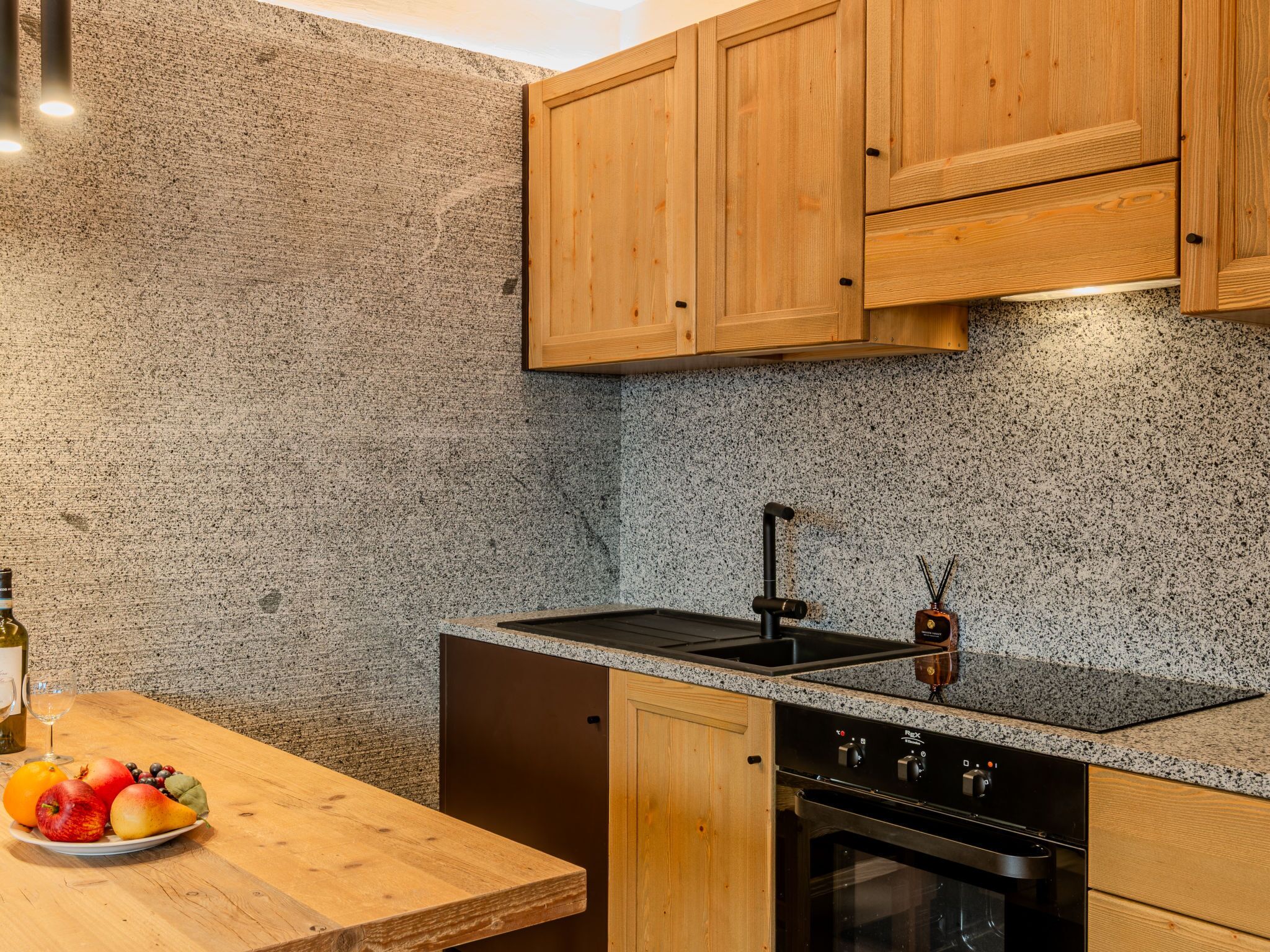 Een keuken met granieten aanrechtbladen, houten kastjes, een zwarte kookplaat en een spoelbak.