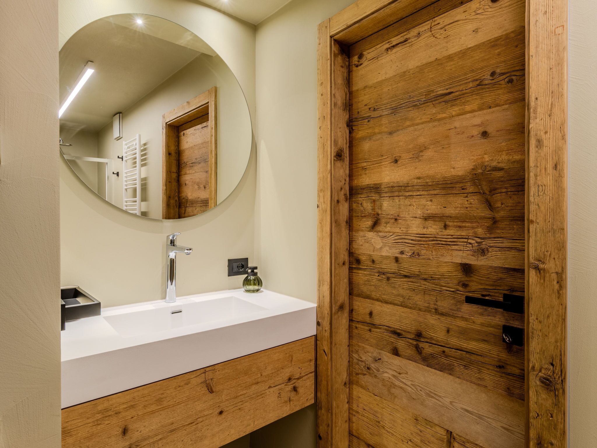 Een badkamer met een witte wastafel, een spiegel en houten lambrisering.