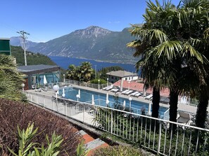 Un espace piscine avec des chaises longues, un bâtiment doté d’un toit rouge et une chaîne de montagnes en arrière-plan.