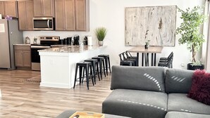 A modern living room with a grey sectional sofa, a wooden tray, and a remote control on a grey ottoman.