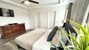 A bedroom with a bed, dresser, ceiling fan, and a plant.