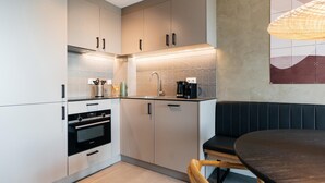 A modern kitchen with stainless steel appliances, a black countertop, and a dining area with a dark table and wooden chairs.