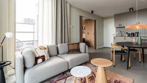 A modern living room with a grey sofa, a round wooden table, and a dining area with chairs.