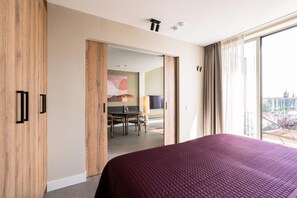 A modern hotel room with a large bed, a dining area, and a view of the cityscape.