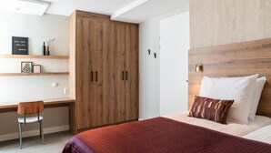 Un dormitorio moderno con un armario de madera, un escritorio con una silla y una cama con una colcha roja.