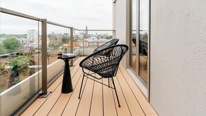 A balcony with a view of a cityscape, featuring two black chairs and a small table.