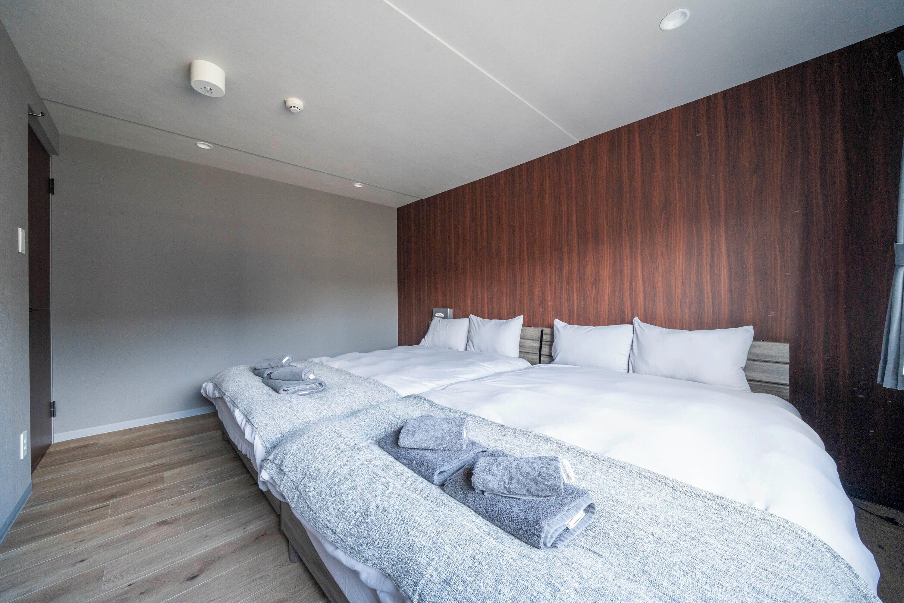 A modern hotel room with a large bed, wooden panel wall, and a wooden floor.