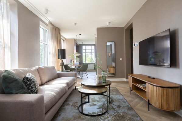 A modern living room with a sofa, coffee table, TV stand, and a dining area with chairs and a table.