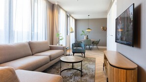 En moderne stue med sofa, sofabord og tv. I baggrunden ses et spiseområde med stole og bord.
