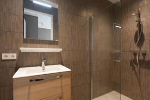 A modern bathroom with a glass-enclosed shower, a white sink with a wooden vanity, and a mirror above the sink.