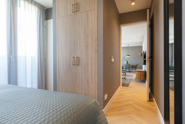A modern bedroom with a large bed, a wardrobe, and a view into a dining area.