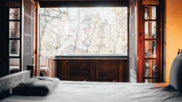 Ein Schlafzimmer mit großem Fenster, einem Bett und einem Holzkasten.