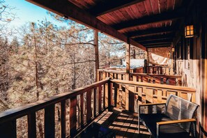 Una baita di legno con un portico, una sedia e vista sulla foresta circostante.