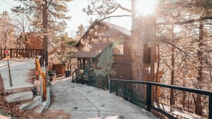 Une cabane avec un escalier menant à l’entrée, entourée d’arbres et d’une clôture en bois.