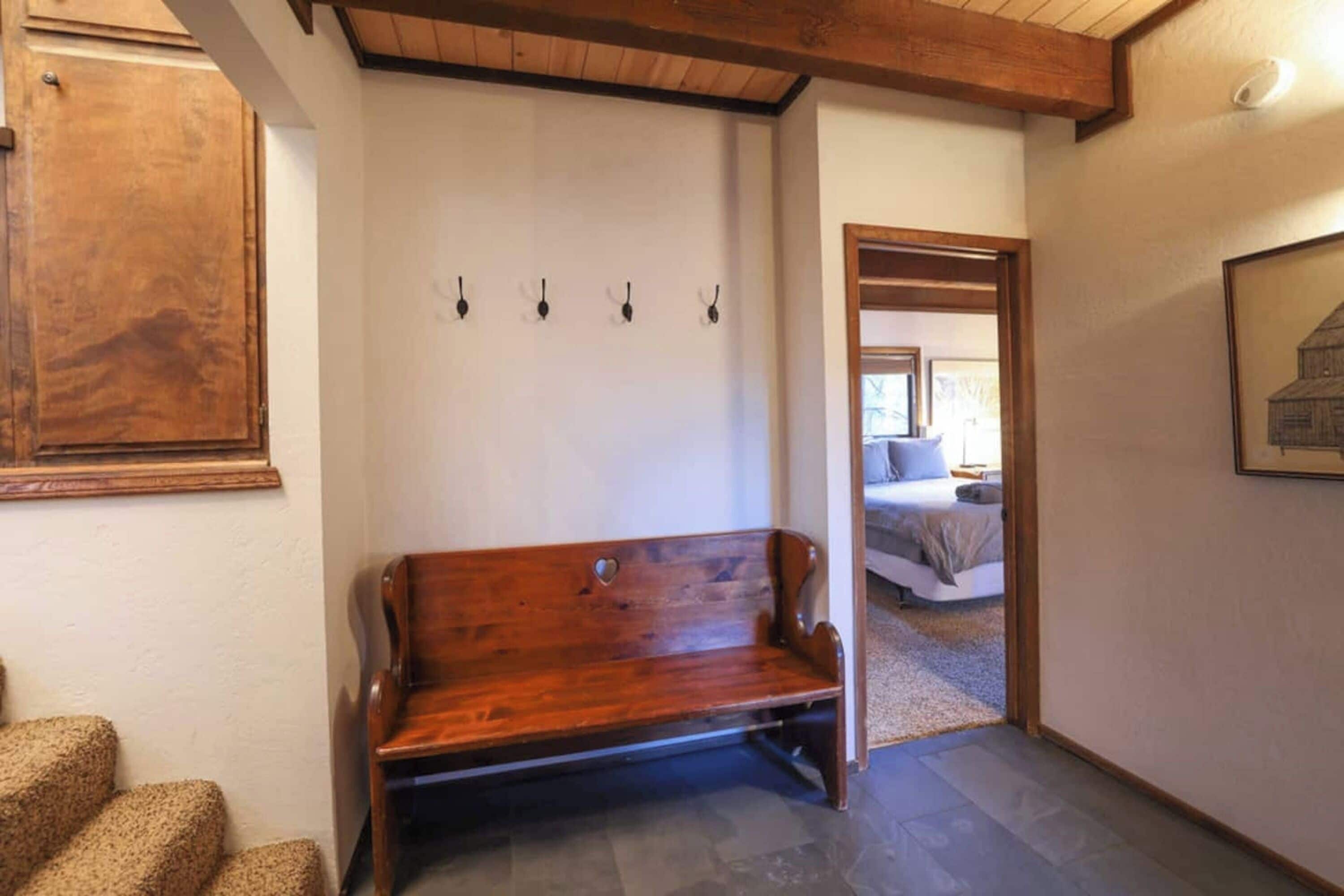Un banco de madera en un pasillo, con un perchero y una puerta que da a un dormitorio.