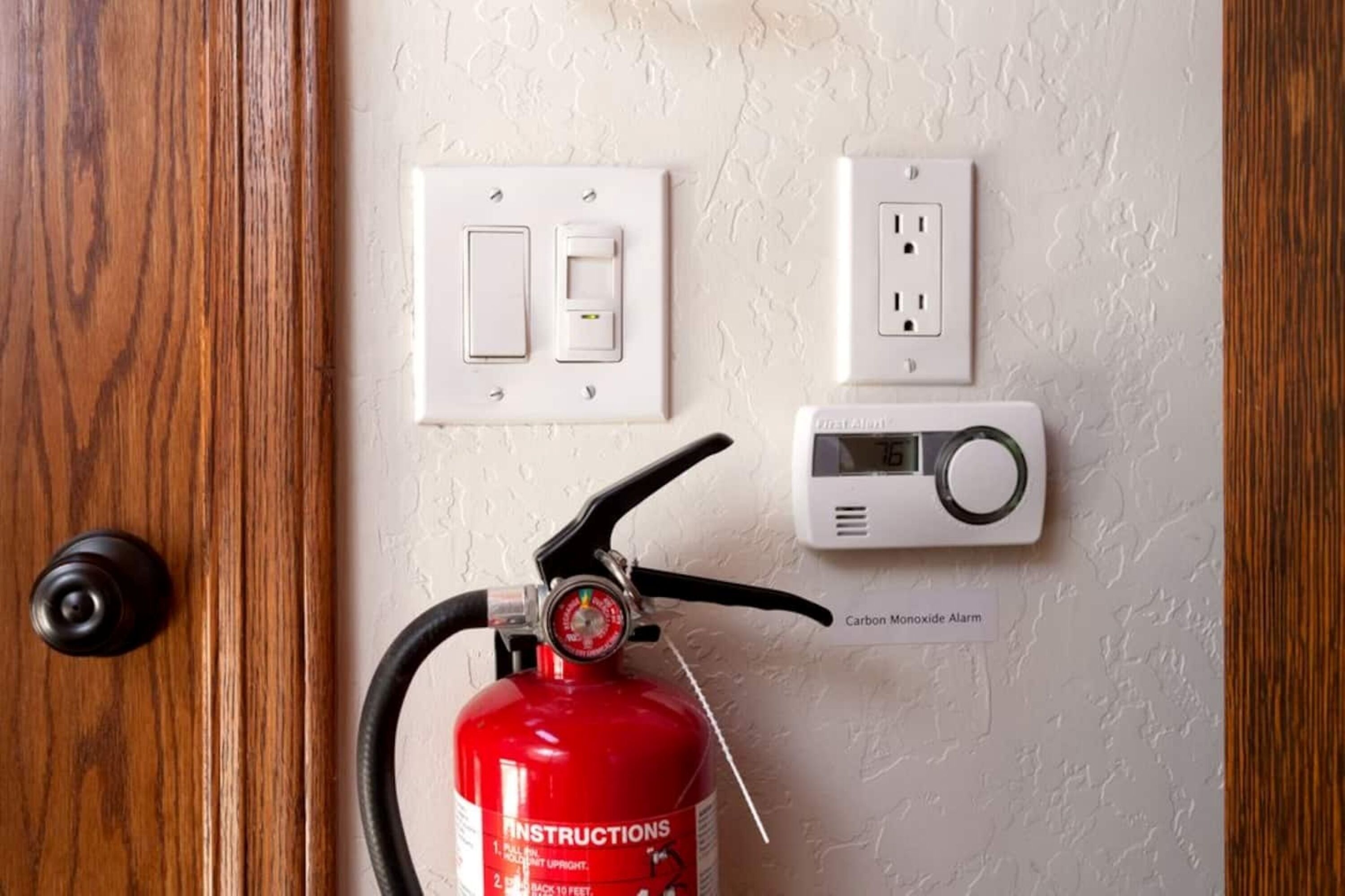 Ein an der Wand befestigter Feuerlöscher mit Kohlenmonoxidmelder und Steckdosen.