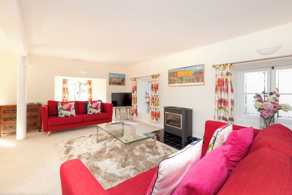 A living room with a red sofa, a glass coffee table, a fireplace, and floral curtains. - Secluded Brewery Apartment   (Edinburgh)