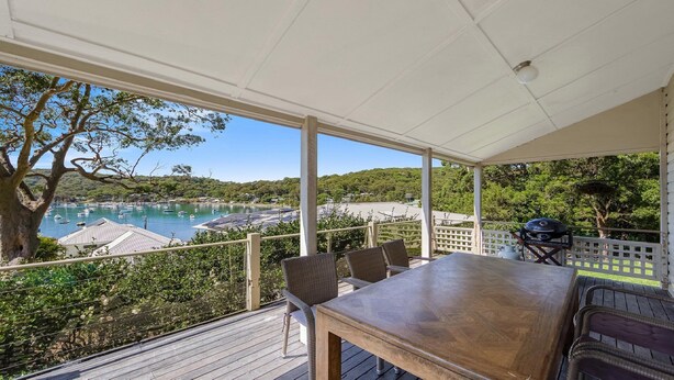 Un espacio al aire libre techado con una mesa y sillas de madera, con vistas a un puerto deportivo con barcos y un paisaje montañoso.