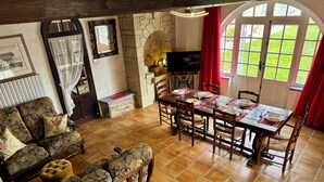 A cozy living room with a stone fireplace, a dining table set for four, and a comfortable sofa. - L'Esprit d'Autrefois - authentic guest house (Cublac)