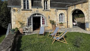 A stone building with a large arched entrance, outdoor seating area with striped chairs, and a well-maintained lawn. - L'Esprit d'Autrefois - authentic guest house (Cublac)