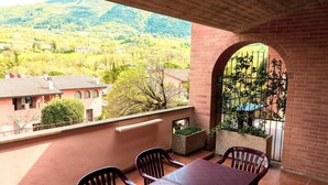 A balcony with a table and chairs, a view of a mountainous landscape, and a brick wall with an archway. - Holiday Home near Assisi with Pool (Assisi)
