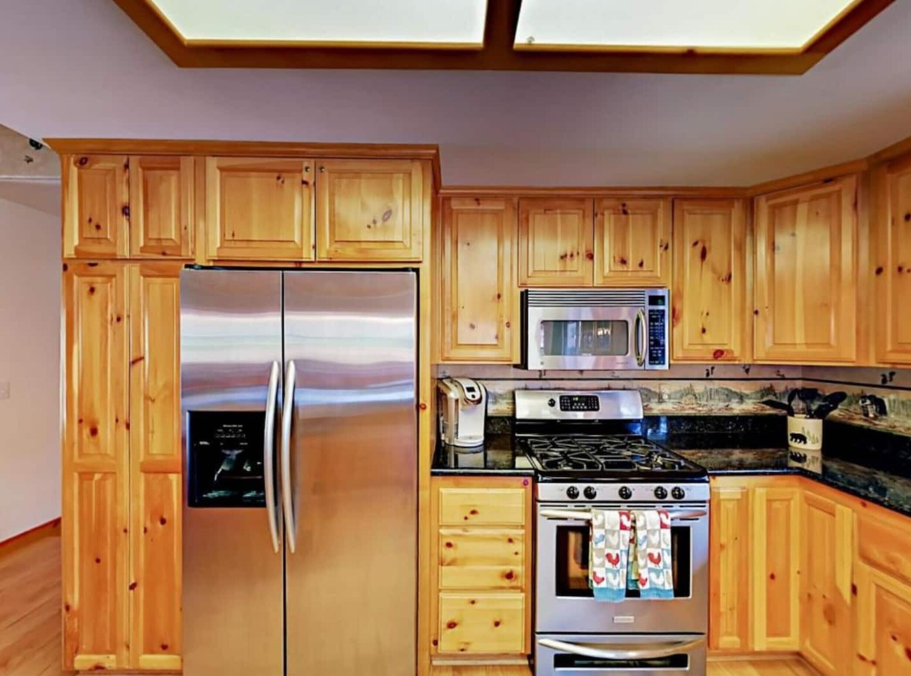 Une cuisine dotée de meubles en bois, d’un réfrigérateur en acier inoxydable, d’un four à micro-ondes, d’une cuisinière et d’un four traditionnel.