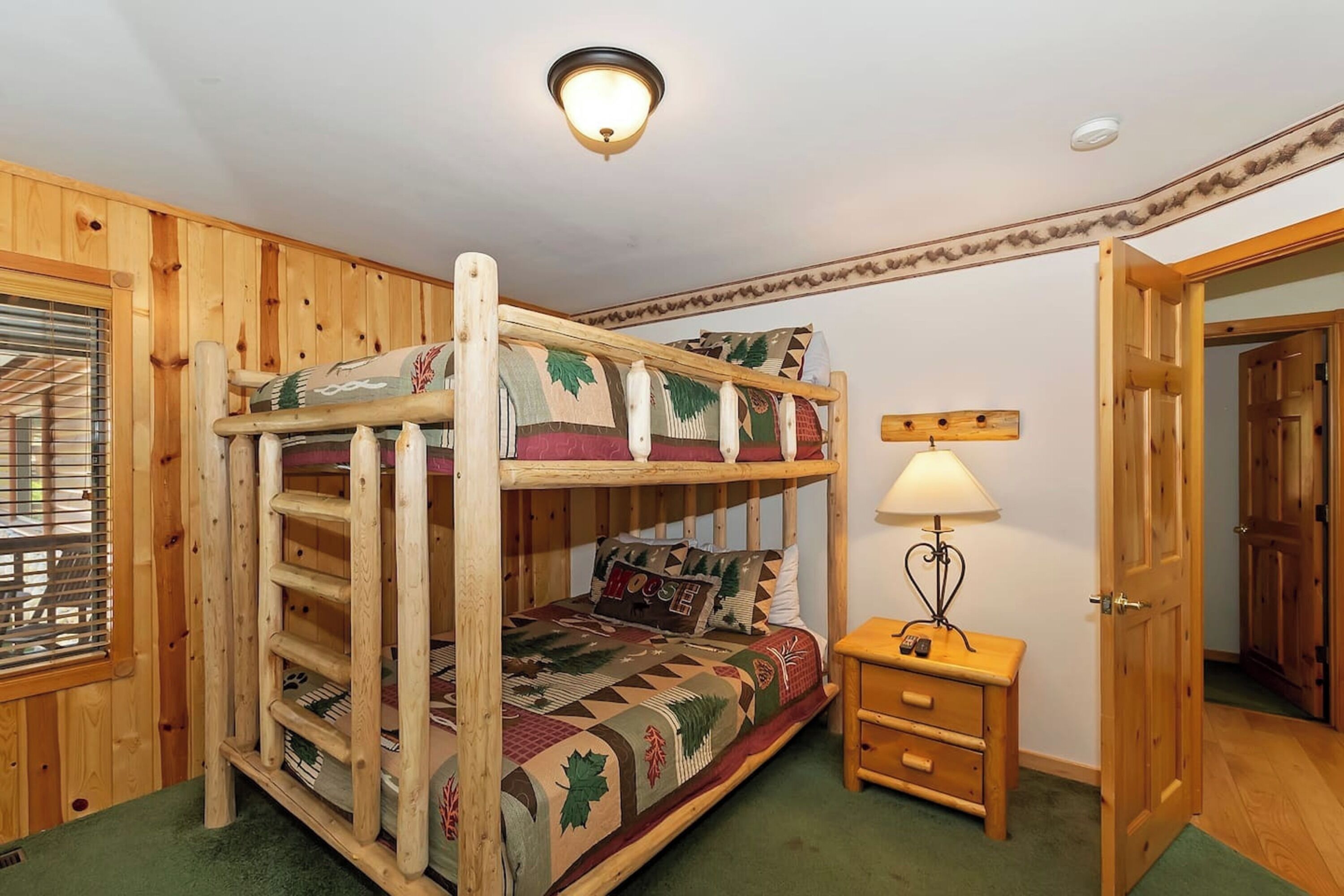 A bunk bed with a ladder, a bedside table with a lamp, and a door to another room.
