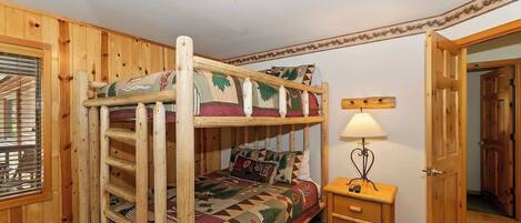 A bunk bed with a ladder, a bedside table with a lamp, and a door to another room.