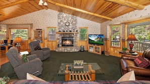 A cozy living room with a stone fireplace, comfortable seating, and a television. - Teakwood Cozy Wood Cabin with Fireplace (Big Bear Lake)