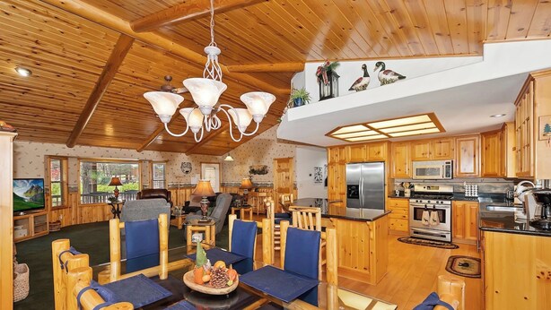 A spacious living area with a wooden ceiling, a chandelier, and a dining table with blue chairs. - Teakwood Cozy Wood Cabin with Fireplace (Big Bear Lake)