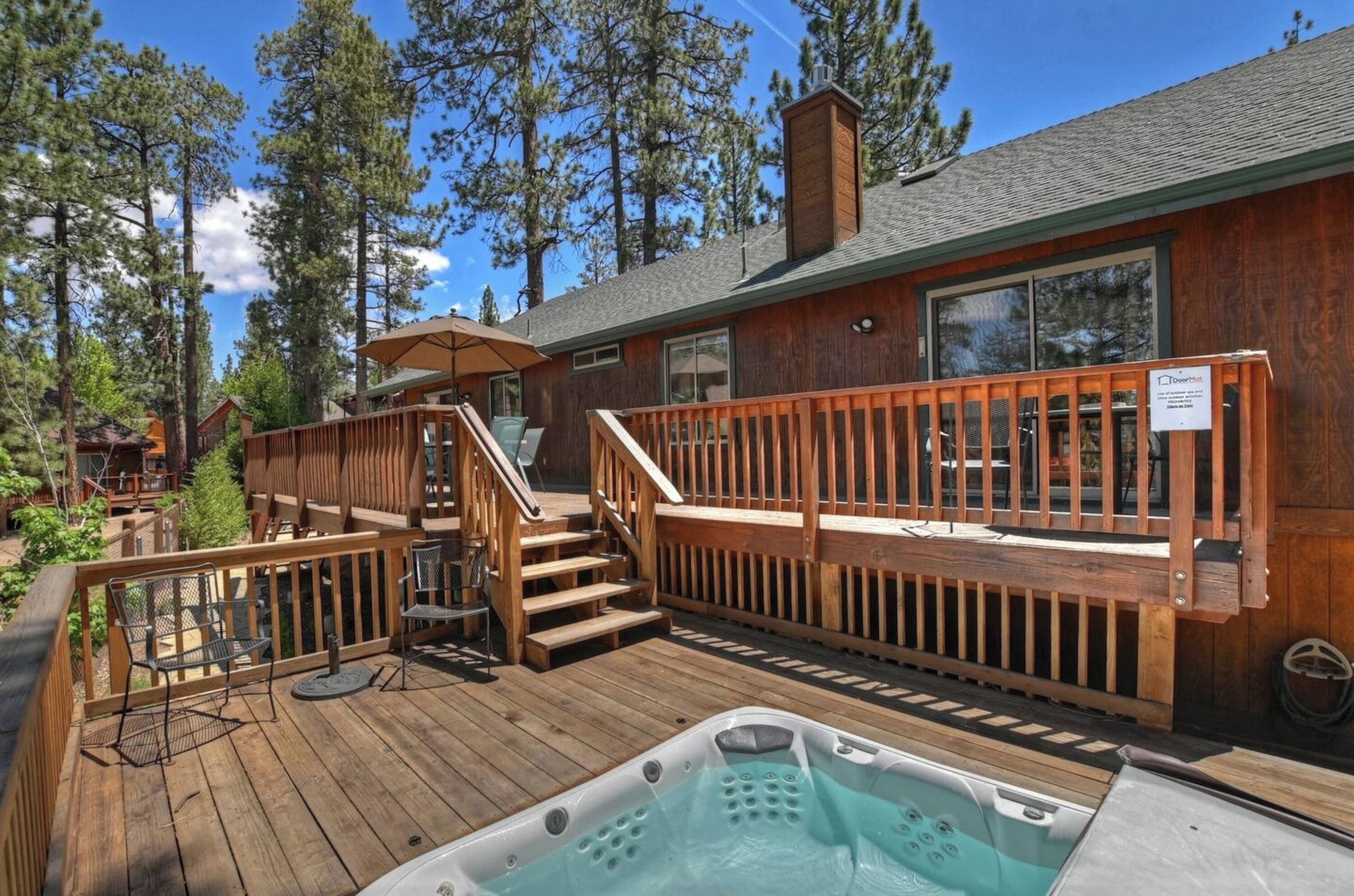 Une terrasse en bois avec un jacuzzi, des sièges d’extérieur et un escalier menant à une zone abritée.