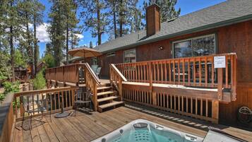 Une terrasse en bois avec un jacuzzi, des sièges d’extérieur et un escalier menant à une zone abritée.