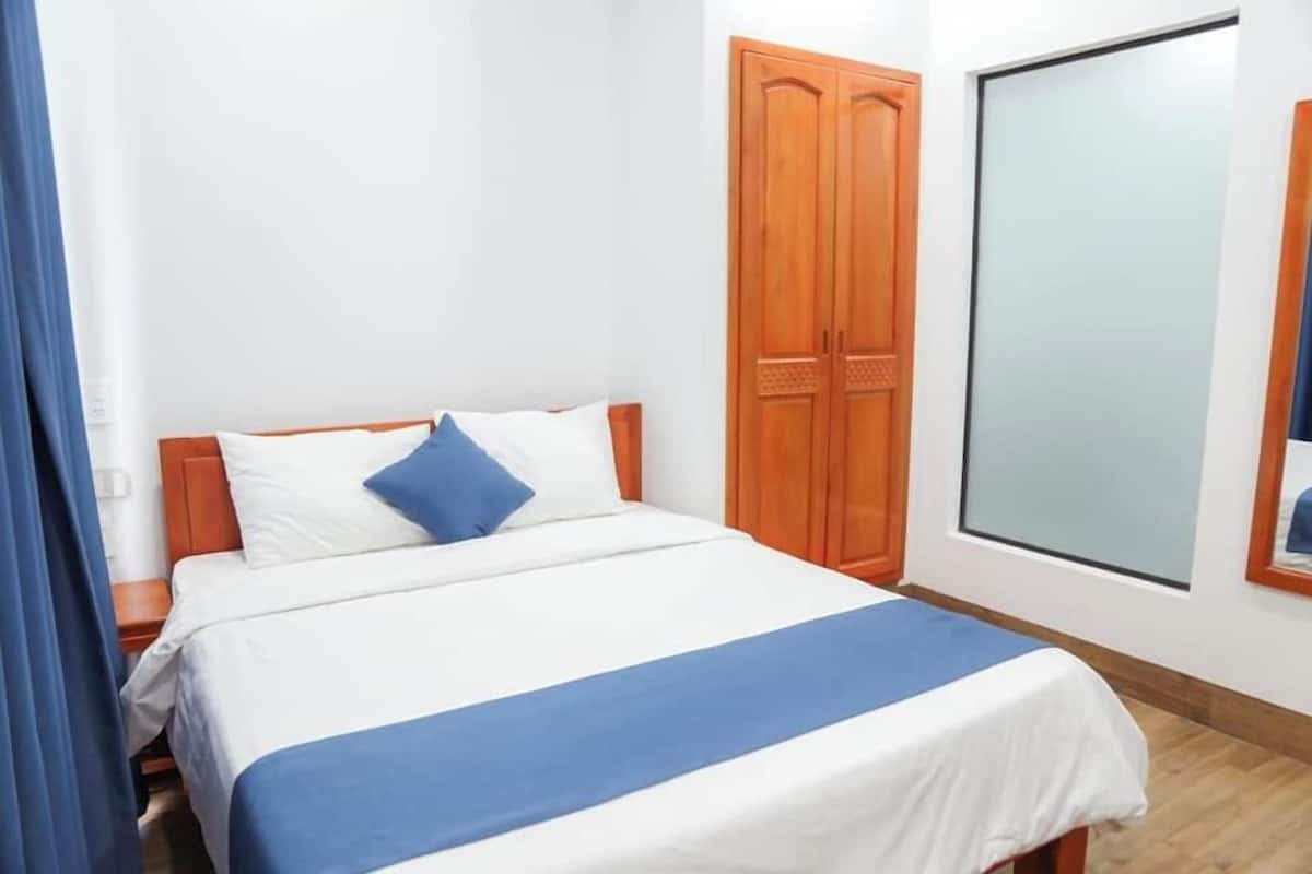 A bedroom with a bed, wooden wardrobe, and a large mirror.