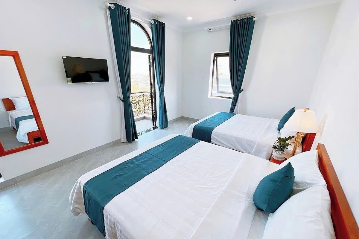 A hotel room with two beds, a TV, a balcony, and a window with curtains.