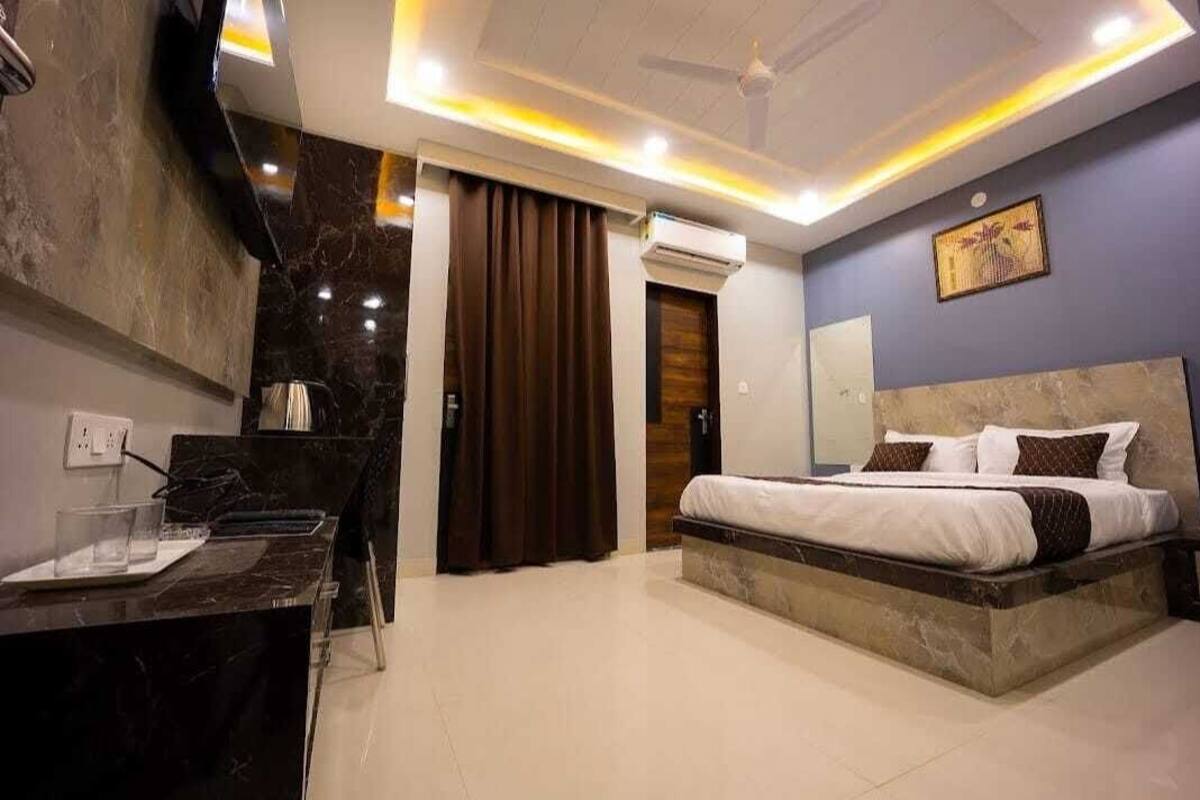 Ein modernes Hotelzimmer mit Marmorboden, einem Bett mit weißer Bettwäsche und braunen Kissen, einem Schreibtisch mit Stuhl und einer Klimaanlage.