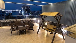 Une terrasse sur le toit avec un espace repas, une balançoire en bois et une vue sur le paysage urbain la nuit.