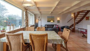 A dining area with wicker chairs and a table, a sofa, and a staircase in the background.