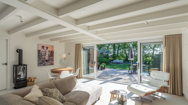 Una sala moderna con un sofá, una mesa y una chimenea. Hay una puerta corrediza de vidrio que da a un patio exterior con jardín y una mesa.